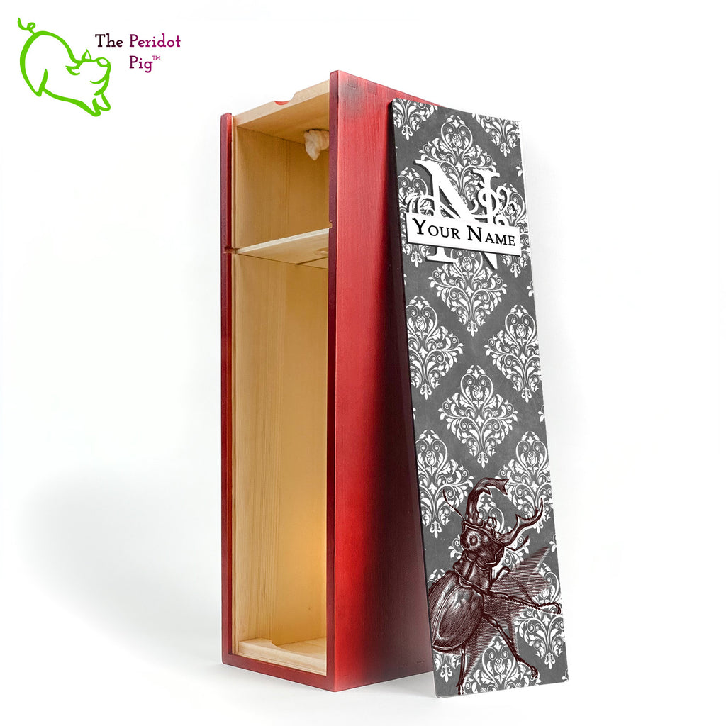 The wine box front panel is decorated in a glossy, detailed print with a white monogram and space for a customized name. This model has a gray background with white decorative scroll work. In the foreground is a large burgundy line drawing of a rhinoceros beetle. Cherry version with the interior shown.