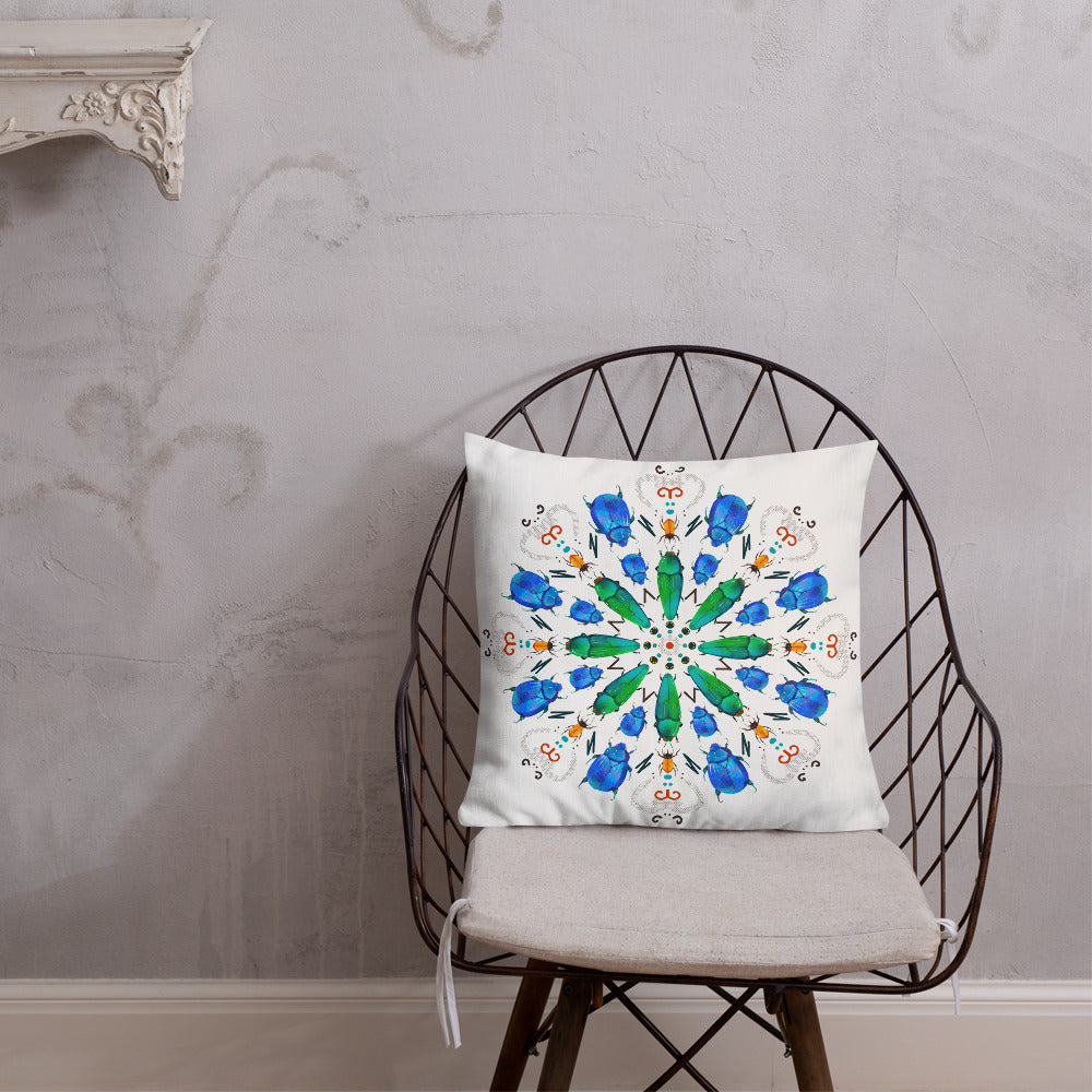 A colorful mandala of beetles graces this white pillow and is availble in either 18"x18" or 22"x22" sizes. The image is printed on both the front and back. The center beetles have shades of bright green.  The smaller beetles are blue and orange. 18" front view shown on a chair.