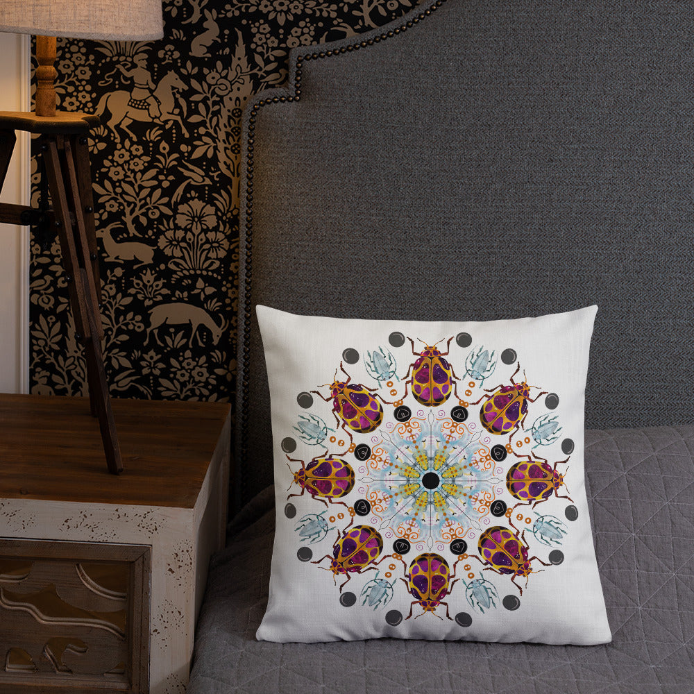 A colorful mandala of beetles graces this white pillow. The larger beetle has shades of violet surrounded by gold. The smaller beetle is in a delicate shade of blue. Printed on a bright, white casing these bugs really pop! Shown in size 18"x18" on a couch.