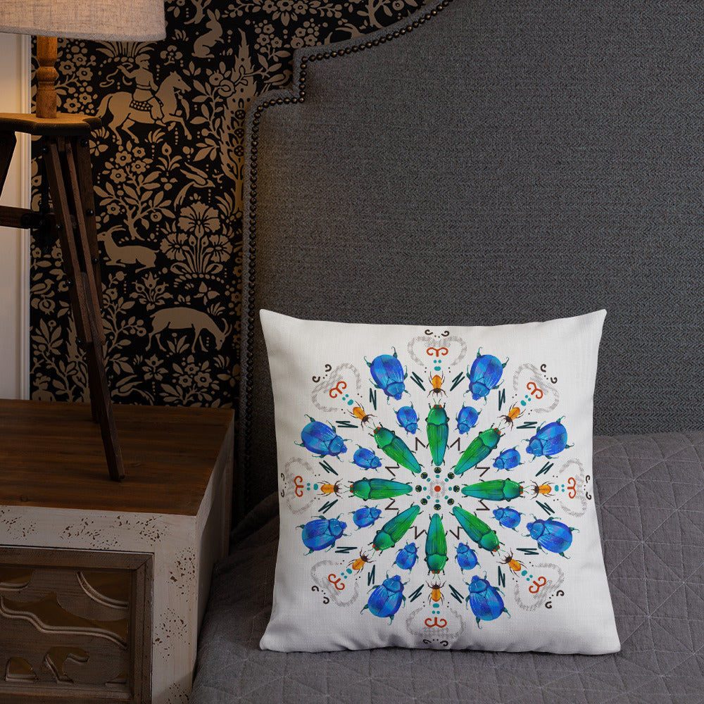 A colorful mandala of beetles graces this white pillow and is availble in either 18"x18" or 22"x22" sizes. The image is printed on both the front and back. The center beetles have shades of bright green.  The smaller beetles are blue and orange. 18" front view shown on a bed.