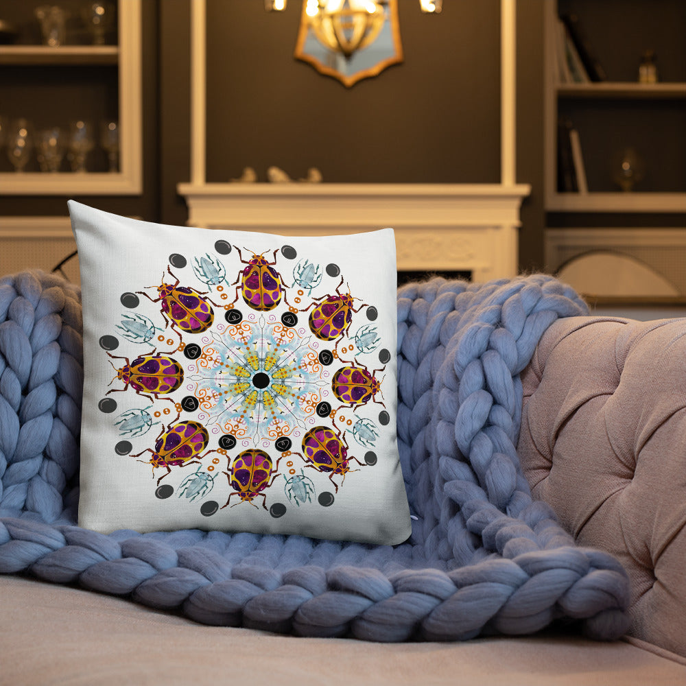 A colorful mandala of beetles graces this white pillow. The larger beetle has shades of violet surrounded by gold. The smaller beetle is in a delicate shade of blue. Printed on a bright, white casing these bugs really pop! Shown in size 18"x18" on a couch against a throw blanket.