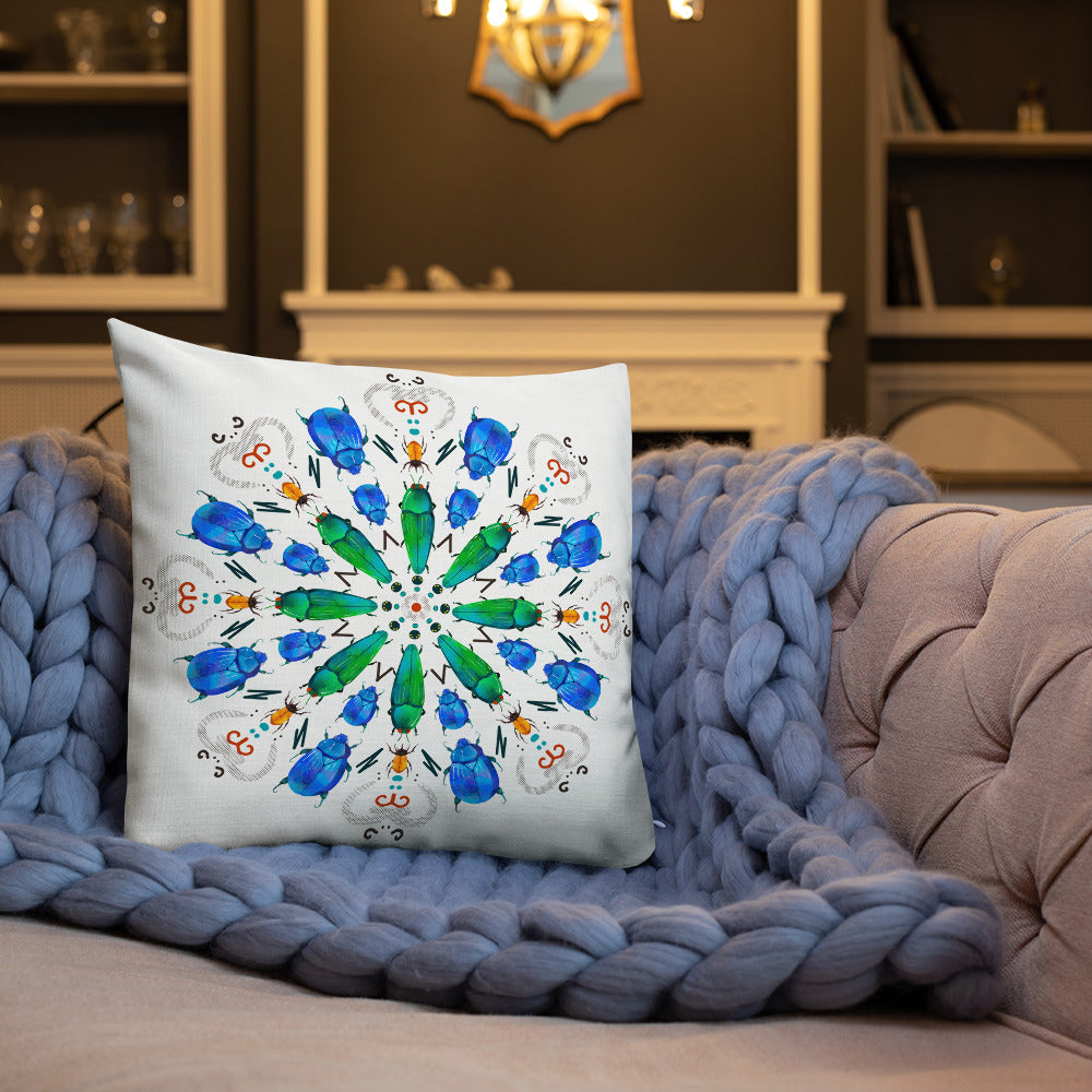 A colorful mandala of beetles graces this white pillow and is availble in either 18"x18" or 22"x22" sizes. The image is printed on both the front and back. The center beetles have shades of bright green.  The smaller beetles are blue and orange. 18" front view shown on a couch.