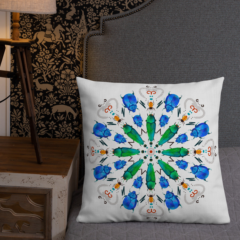 A colorful mandala of beetles graces this white pillow and is availble in either 18"x18" or 22"x22" sizes. The image is printed on both the front and back. The center beetles have shades of bright green. The smaller beetles are blue and orange. 22" front view shown on a bed.