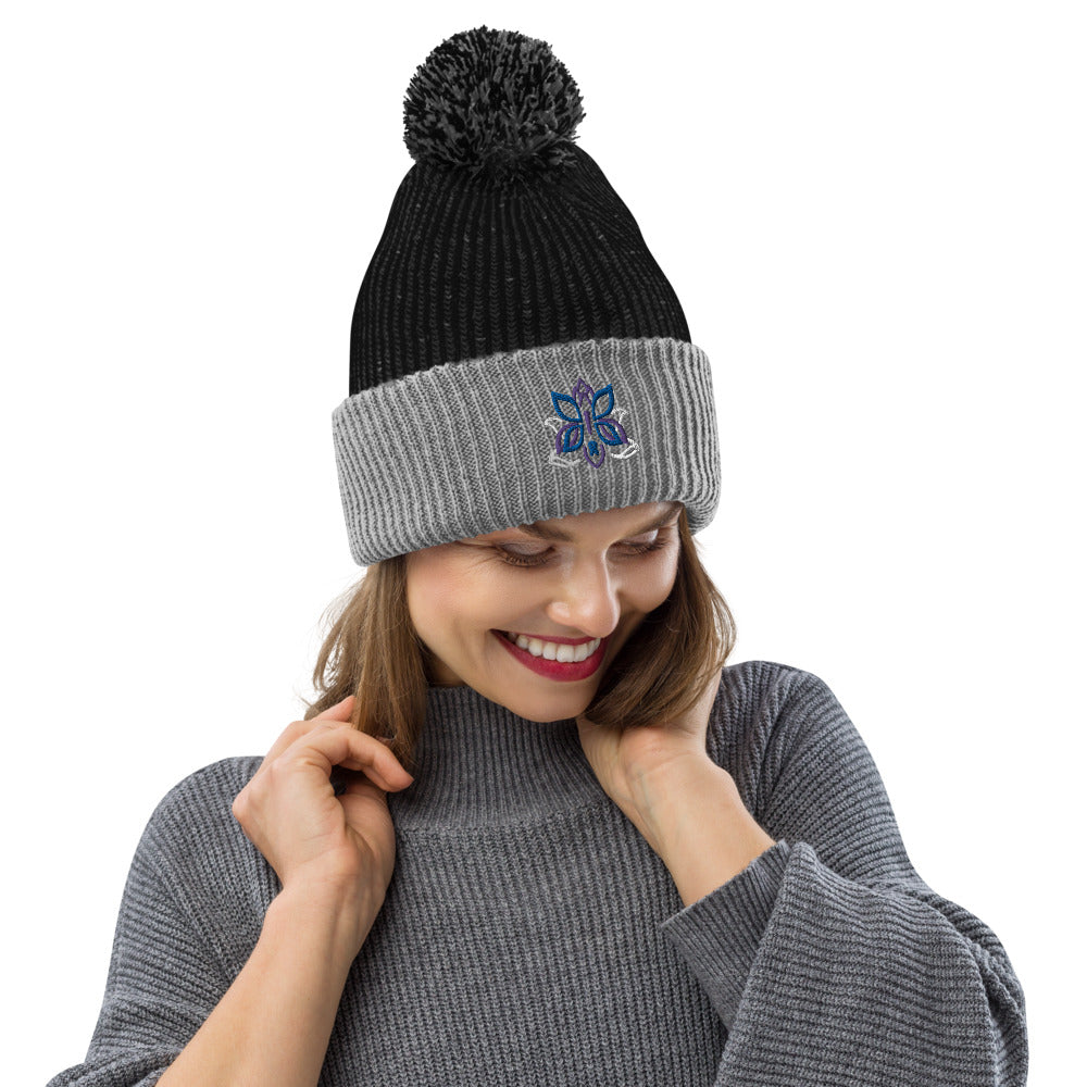 A model wearing a comfy, cozy pom-pom beanie in gray and black featuring the Kristin Zako logo